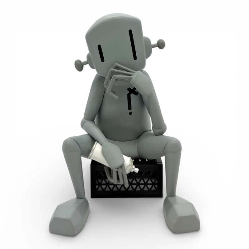 Gray robot sitting on a black box with a white object inside against a white background