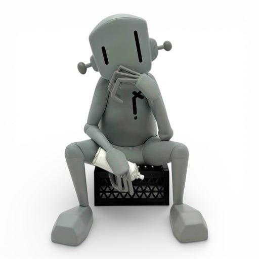 Gray robot sitting on a black box with a white object inside against a white background